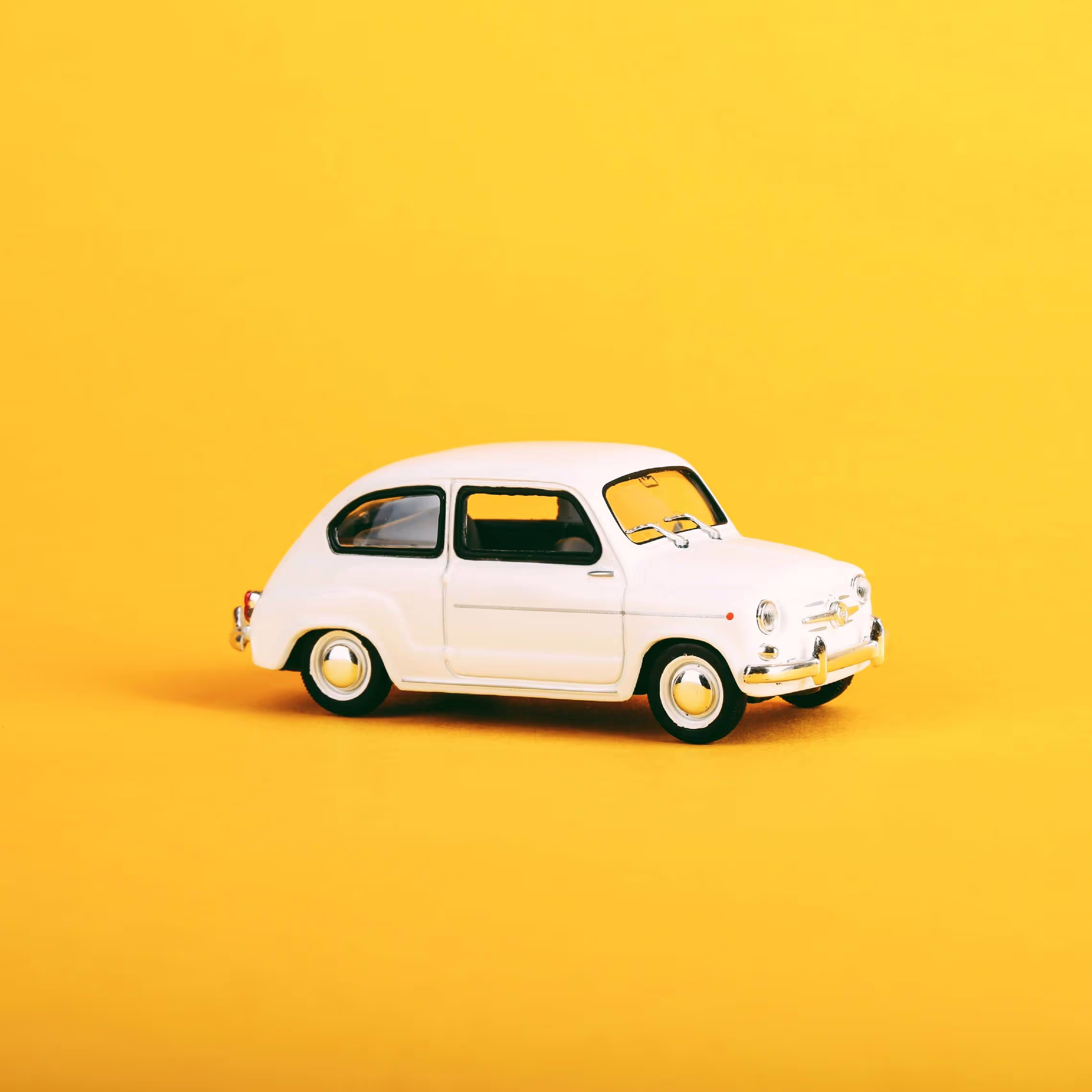 A small white toy car on a yellow background